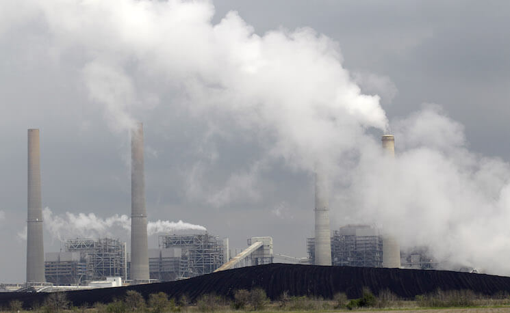 Exhaust rises from smokestacks in front of piles of coal at NRG Energy's W.A. Parish Electric Generating Station in Thompsons, Texas