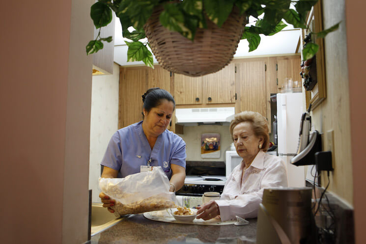 Home health aide Maria Fernandez, left, pours cereal for Herminia Vega, 83, right, as she performs household chores for Vega and her husband.
