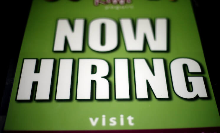 A "Now Hiring" sign appears in a storefront display window in Philadelphia. 