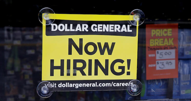 A "Now Hiring" sign hangs in the window of a Dollar General. 