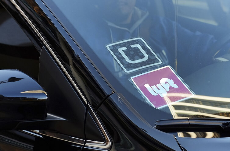 A driver displaying Lyft and Uber stickers on his front windshield drops off a customer in downtown Los Angeles.