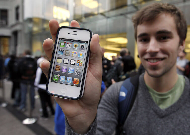 Elliott Johns, of Boston, holds up an iPhone 4S in front of an Apple Store location in Boston.