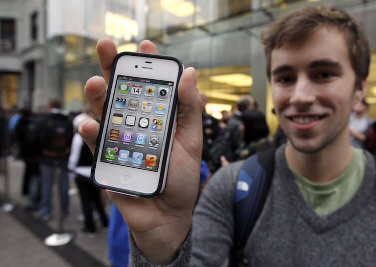 Elliott Johns, of Boston, holds up an iPhone 4S in front of an Apple Store location in Boston. 