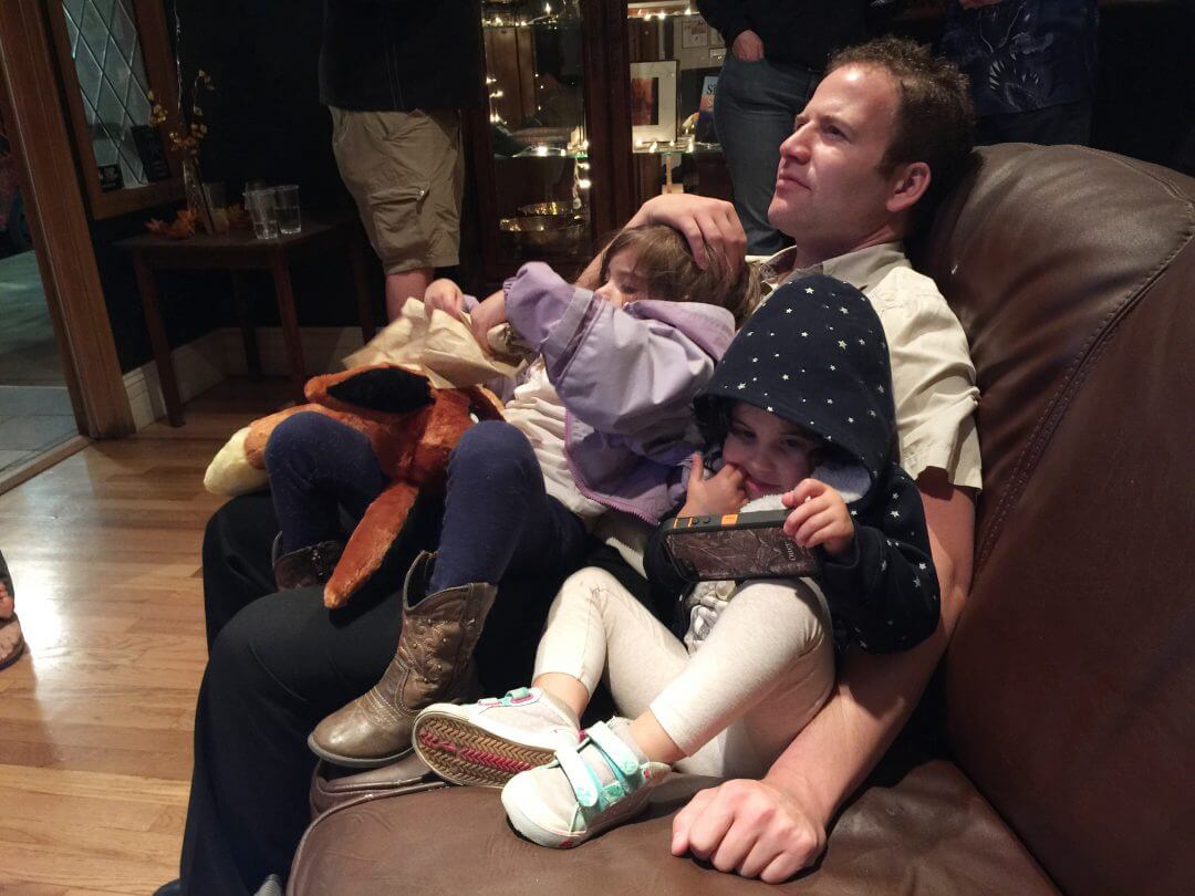 A father watches television with his daughters in Denver. 