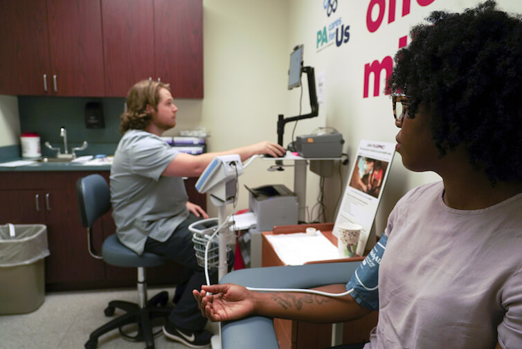 A research technician at the University of Pittsburgh Medical Center collects blood pressure data from a patient.