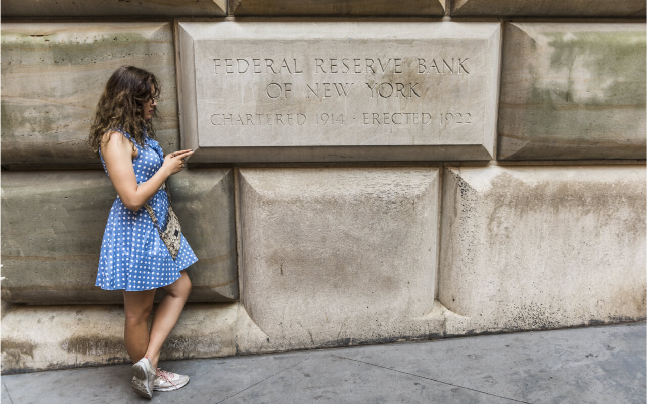 New York, USA - June 18, 2016: A young woman checks her phone in front of the Federal Reserve Bank of New York.